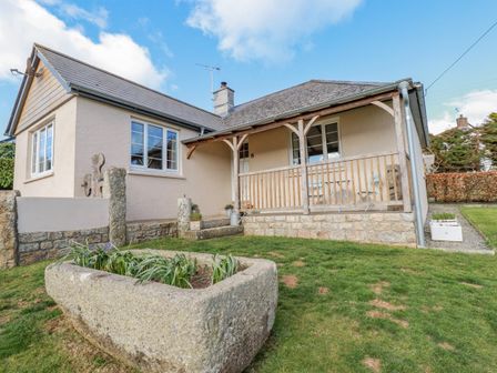 An exterior view of a house with a covered porch and stone planter in the grassy yard at Penlaurel Crackington Haven Near Bude