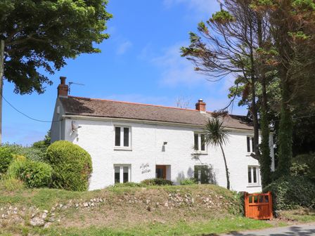 A white two story house with multiple windows a satellite dish and trees at Myrtle Cottage in Hayle