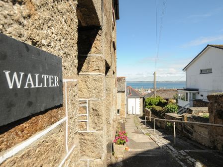 A narrow street with stone buildings flowers and a view of the sea at Walter in Newlyn