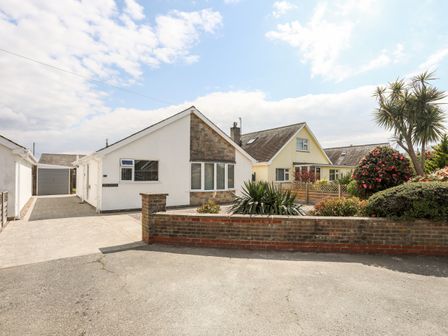 A driveway leading to a white bungalow with adjacent garden and neighboring house at 31 Beach Road in Morfa Bychan