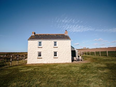 An exterior view of a stone cottage with four windows and a chimney on a grassy field at Faraway Cottage in St Levan near Porthgwarra