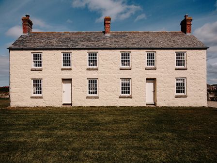 A stone house with two doors and eight windows on a lawn at Three Chimneys in St Levan near Porthgwarra