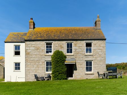 A stone house with chimneys and outdoor furniture on grass at Higher Roskestal in St Levan near Porthgwarra
