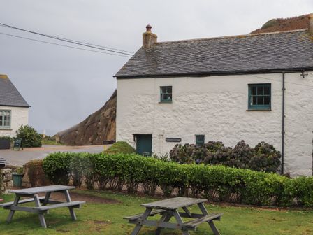 Stone cottage with green windows and hedges with picnic tables on grass at Corner Cottage in Porthgwarra