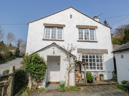 A white two story house with large windows plants and firewood at The Old Post House in Witherslack