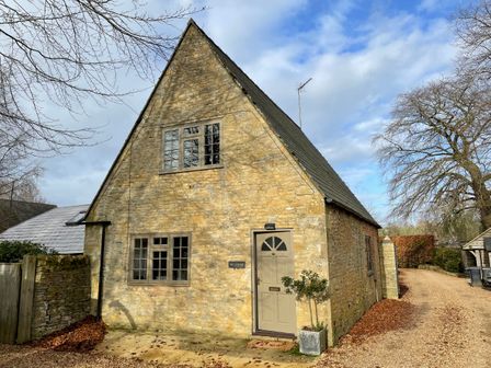 A stone cottage with a peaked roof and two front windows at Omas Cottage Moreton-In-Marsh