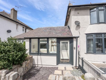 The exterior of a semi detached house with a glass door and windows a small garden with stone pathway and plants at Beeches Bach in Prestatyn