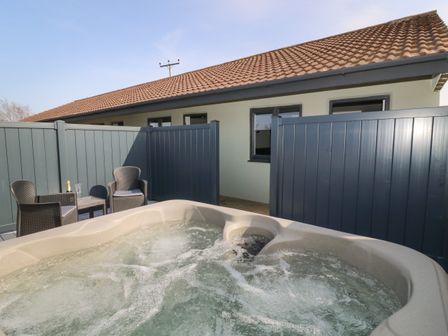 An outdoor hot tub with bubbling water next to two chairs and a table on a patio at Chalet 5 in Sherburn