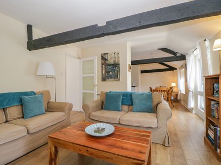 A living room with two sofas, wooden coffee table, floor lamp, wall art, and dining area with wooden table and chairs at The Old Mill in Keswick