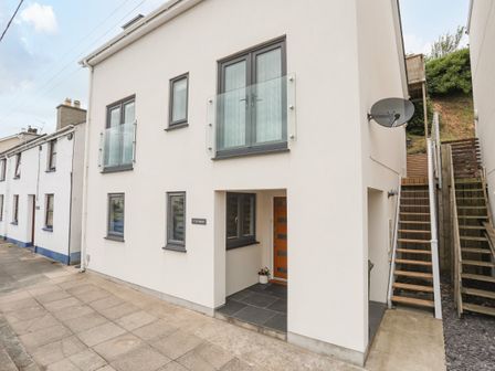 The exterior of a modern white house with grey framed windows glass panels and stairs leading up to a door at 3 Ty Stabal in Pwllheli