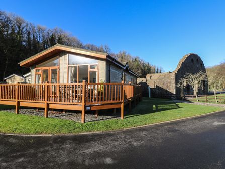 A single-story wooden cabin with a deck and railing next to stone ruins on grass at Seventh Heaven in Wisemans Bridge