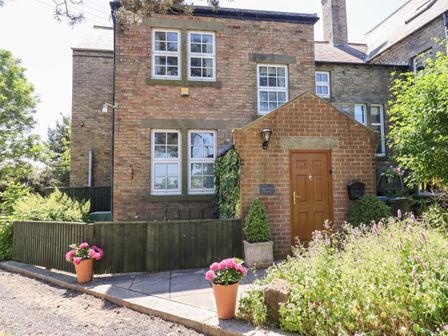The exterior of a brick house with a wooden front door flanked by potted plants and surrounded by greenery at Buzzards Rest in Stannington near Morpeth