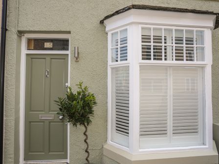 A green front door next to a bay window with white shutters and a small spiral shaped tree at 15 Rosemary Lane in Beaumaris