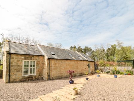 A stone cottage with a paved path and potted plants in a gravel yard at Kizzie Cottage in Guyzance near Warkworth