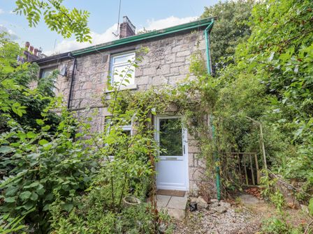 A stone cottage with a white door surrounded by greenery and plants at 26 Llawr Pentre in Old Colwyn