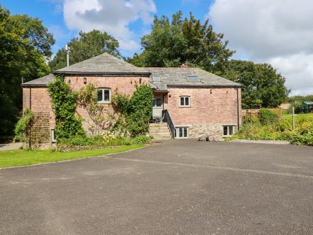 A brick house with stone foundation and plants growing on the walls with a paved driveway and trees in the background at The Old Watermill in St Mabyn