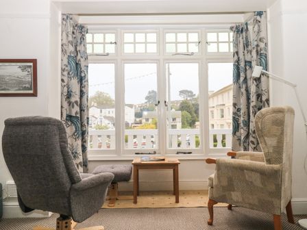 A sitting area with two chairs a small wooden table and floral curtains by a large window at Clarendon House in Dawlish