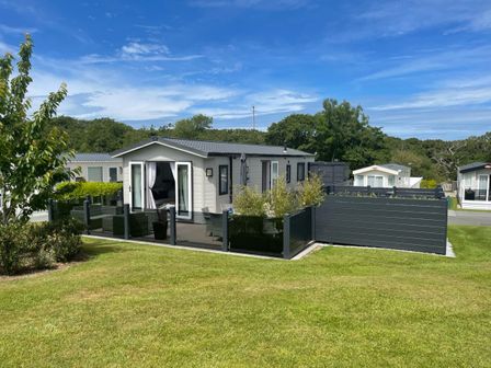 A small modern house with a fenced patio and outdoor seating on a lawn at 97 Crugan in Llanbedrog