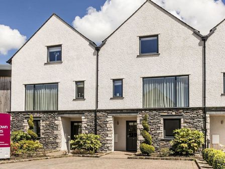 A townhouse exterior with stone and white walls and a paved driveway at Town House 5 at Carus Green Golf Club Kendal