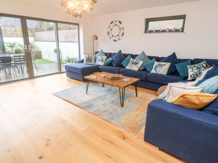 A living room with a large blue sectional sofa with decorative pillows a wooden coffee table on a rug and glass sliding doors leading to an outdoor seating area at Tregenna House in St Ives