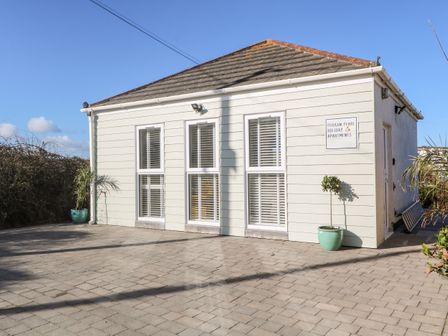 The exterior of a small building with three tall windows and two potted plants on a paved area at Perran Pearl A in Perranporth
