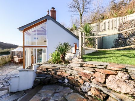 An exterior view of a house with large windows stone walls and a patio with outdoor furniture at Jonwyns in Trewarmett