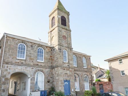 A stone building with arched windows and a tower with louvred openings at 2 Bell Tower in Penzance