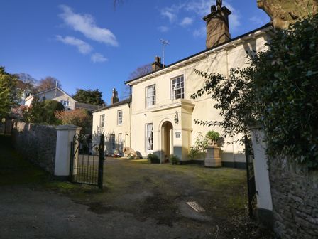 The exterior of a two-story cream coloured house with chimneys a gated entrance and driveway at Clarence Grey House in Torquay