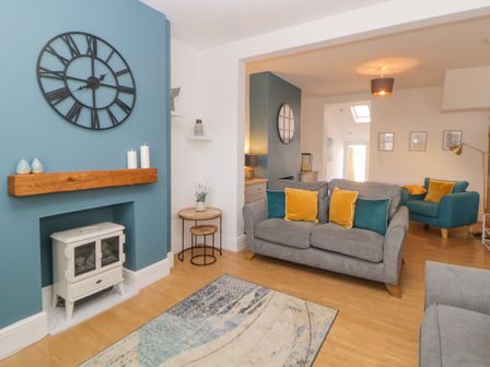 A living room with sofas and pillows near a clock above a fireplace at Keeling in Exmouth