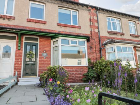 Front view of a brick terraced house with a green door and flower garden at Faran House in Staithes