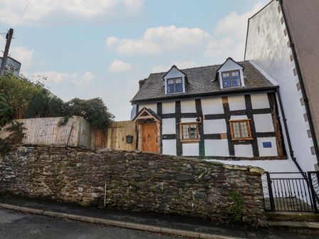 A half-timbered house with two dormer windows behind a stone wall and wooden fence at 18 Church Street in Llangollen