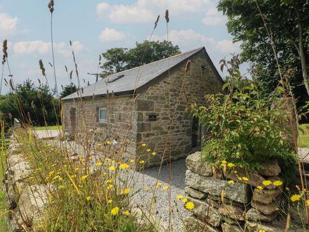 A stone building with a slate roof surrounded by wildflowers and trees at The Reading Room in Seworgan near Constantine
