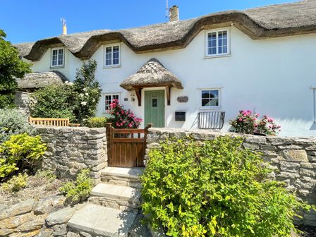Front of a thatched cottage with green door flowers and stone wall at Cajun Cottage in West Lulworth