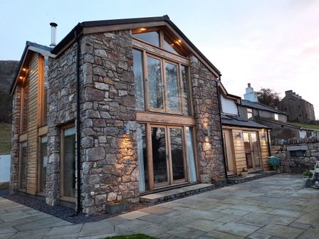 Exterior view of a stone and wood cottage with large windows and a paved patio at Ty Gwyn Cottage in Colwyn Bay