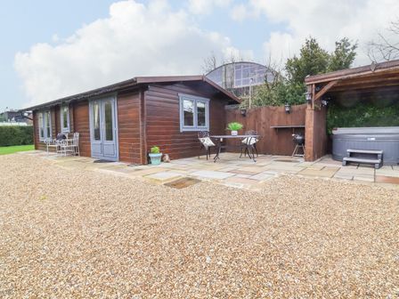 A wooden cabin with outdoor seating and a covered hot tub on a stone patio at Westfield Lodge in Terrington near Sheriff Hutton