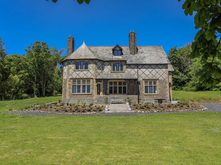 A large stone house with multiple windows chimney and a garden in the front at Bryn Henllan in Criccieth