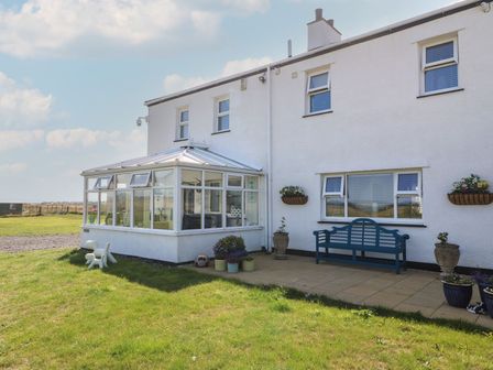 Exterior of a white house with a conservatory blue bench and potted plants on a patio at Trewan House in Bryngwran near Rhosneigr Rhosneigr