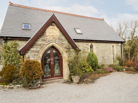A stone building with arched door and stained glass windows surrounded by plants and gravel path at The Chapel in Dol-y-Gaer near Pontsticill