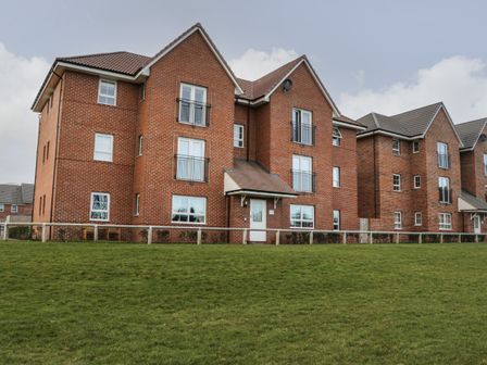 A three-story brick apartment building with multiple windows and balconies overlooking a grassy area at Woodside View in Whitby