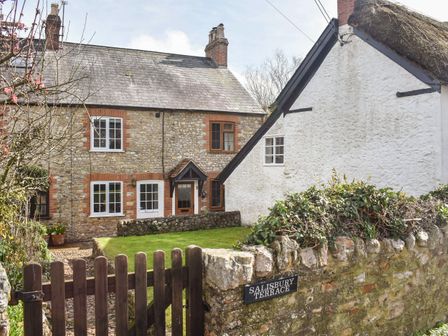 A stone cottage with a wooden gate and a sign reading Salisbury Terrace surrounded by a garden at Jasmine Cottage in Kilmington Devon