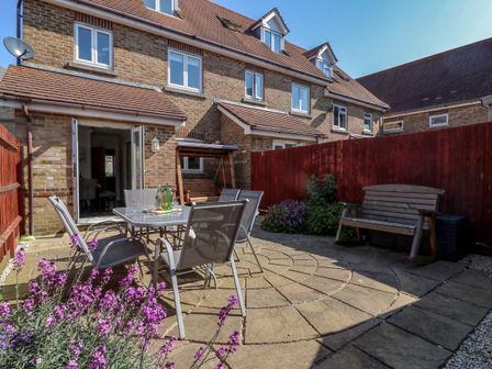 A backyard patio with a glass table and chairs purple flowers a wooden bench and a wooden swing at Anchors Away in Weymouth