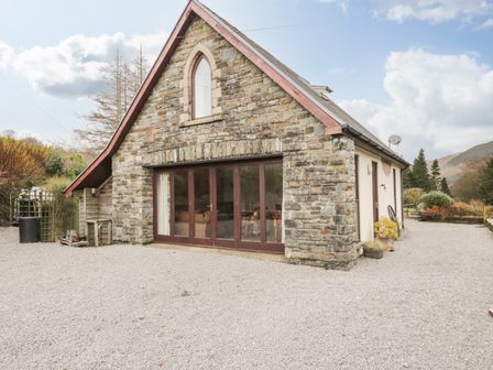 A stone cottage with large glass doors and gravel driveway at The Lodge in Dol-y-Gaer near Pontsticill
