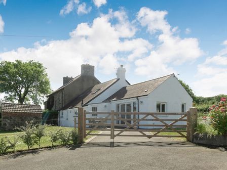 A white single-story house with a wooden gate and outdoor patio furniture at Morlan Cottage in Newport Pembrokeshire