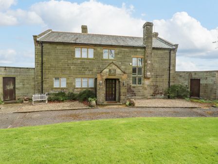 A two story stone house with chimney and front door surrounded by stone walls and green lawn at Aislaby Hall in Aislaby