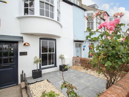 Front exterior of a house with a black door two potted plants and pink flowers in a garden at 6 The Terrace Brewers Quay Harbour
