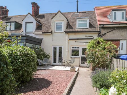 A rear view of a terraced house with a small garden patio and outdoor furniture at 3 St Cuthberts Garth Bamburgh