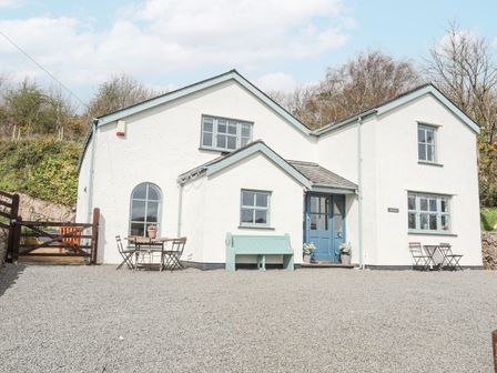 A white house with blue door and windows outdoor tables and chairs on a gravel driveway at Bethania in Llangoed near Beaumaris