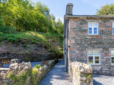 The side of a stone house with white windows and a gravel pathway surrounded by low stone walls and greenery at Cunsey Mill House Cunsey near Hawkshead