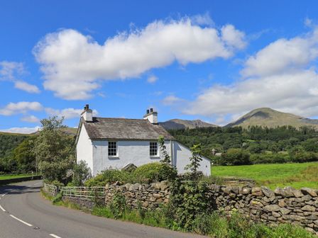 A white cottage near a winding road with stone walls and green fields at Ellis Howe in Torver