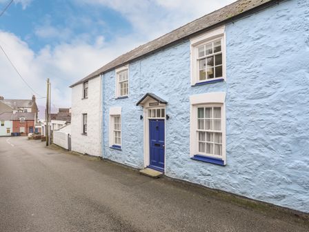 A street view of cottages with blue and white textured walls and blue doors and window frames at Bwthyn Dwyfor in Beaumaris